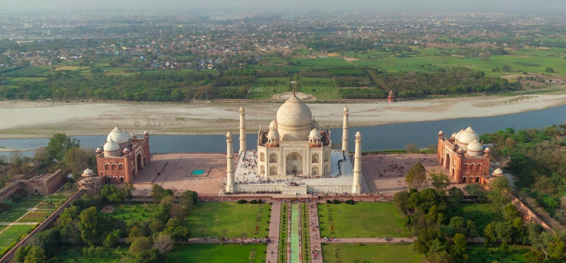 The white marble Taj Mahal in Agra reflected in the central Charbagh garden pool under a clear blue sky.