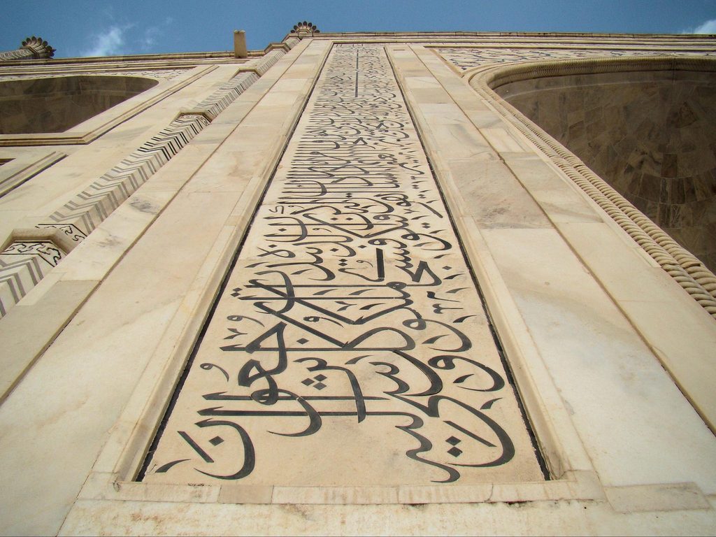 Black marble Arabic calligraphy in Thuluth script inlaid on white marble around the Taj Mahal portal arch.