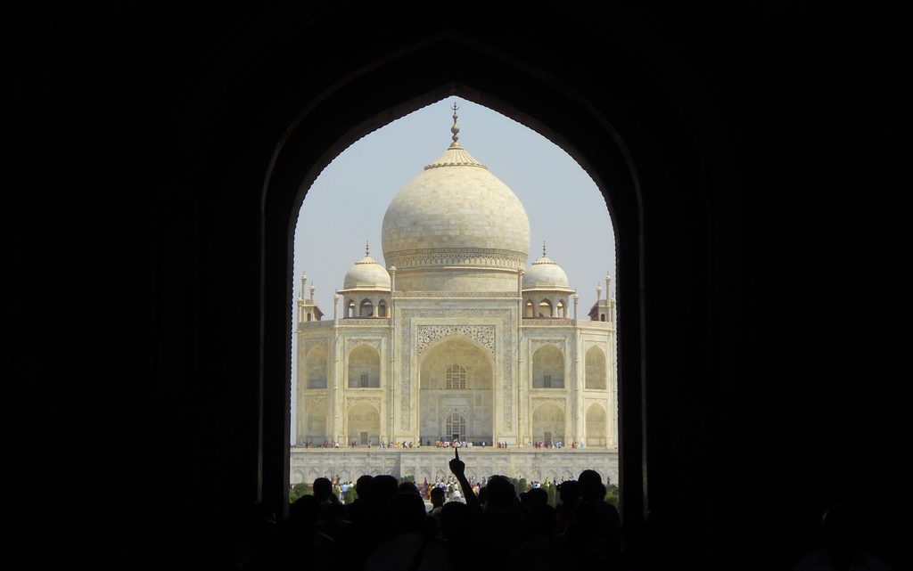 The white marble dome of the Taj Mahal framed through the pointed archway of the Great Gate.